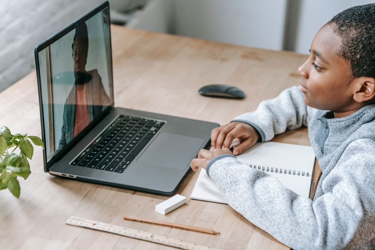 A young boy at a desk in a live video session with his tutor on a laptop
